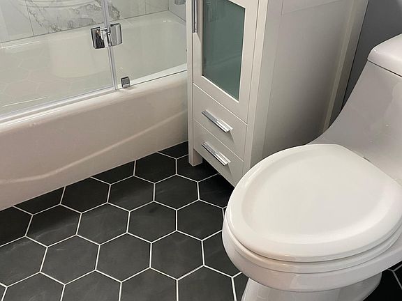 Hexagon tile in bathroom with glass shower door, and large ceramic tile in shower.
