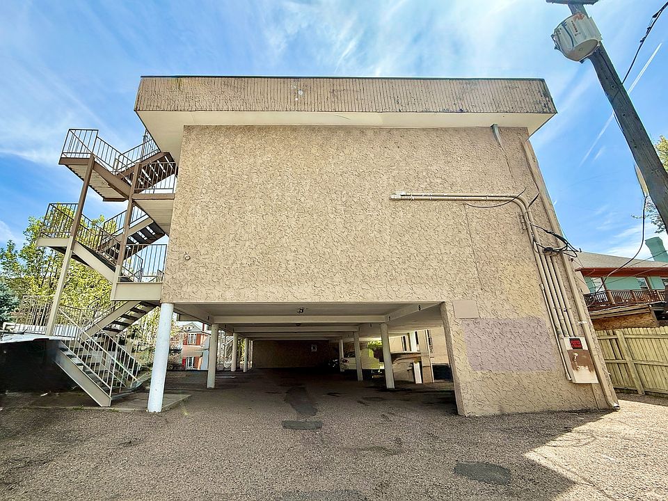 Charming urban apartment complex with stylish external staircase and ample parking under a bright blue sky.