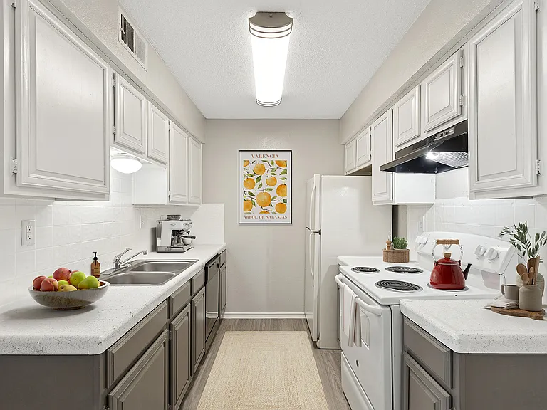 A chef's kitchen is shown with white and black appliances, red tea kettle on stove, and bowl of fruit on the counter.