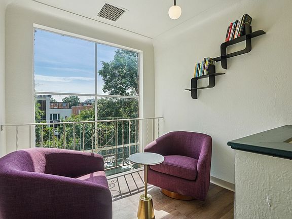 Cozy nook with plush purple chairs and a modern bookshelf, bathed in natural light from a large window overlooking lush greenery.