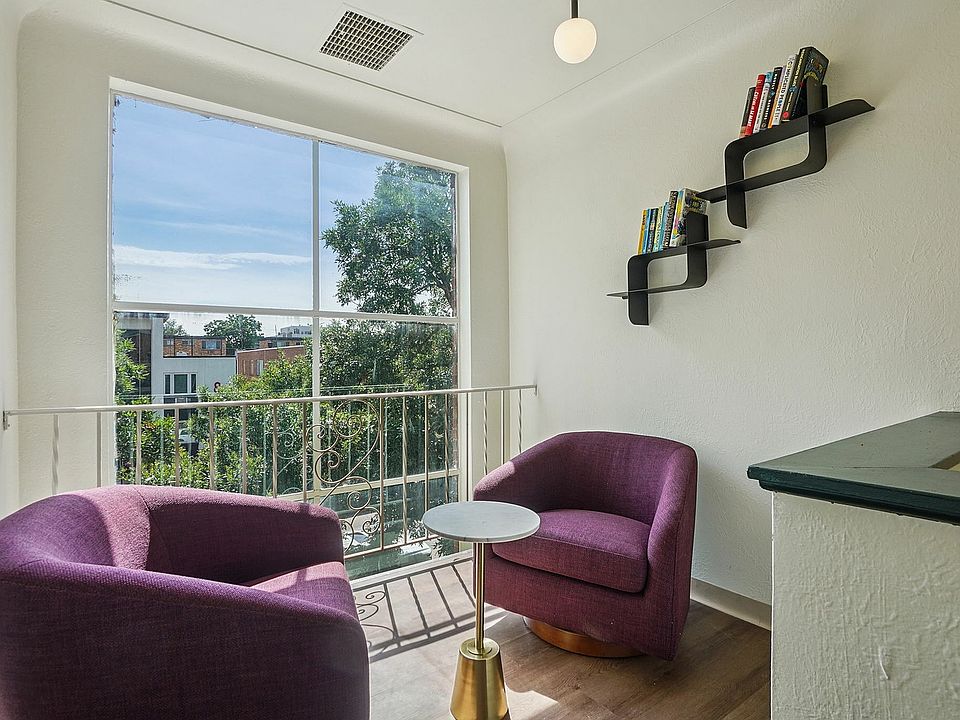 Cozy nook with plush purple chairs and a modern bookshelf, bathed in natural light from a large window overlooking lush greenery.