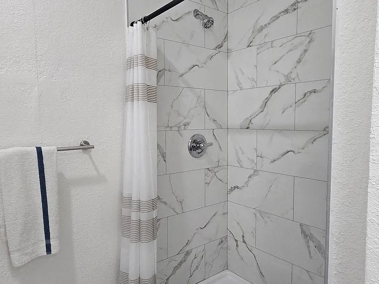 Bathroom features a tiled shower surround with a shower/tub combo, chrome fixtures, and easy-clean flooring.