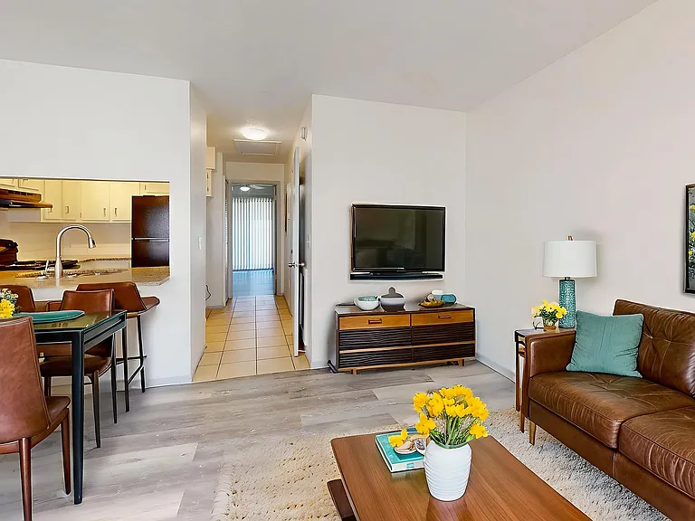 Bright and modern living space with a cozy leather sofa, vibrant yellow flowers, and a sleek TV setup. The open kitchen and dining area promise seamless entertaining.