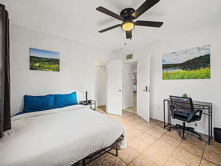 Private bedroom with tile floors, ceiling fan, and furnished work desk, plus closet storage and easy hallway access.