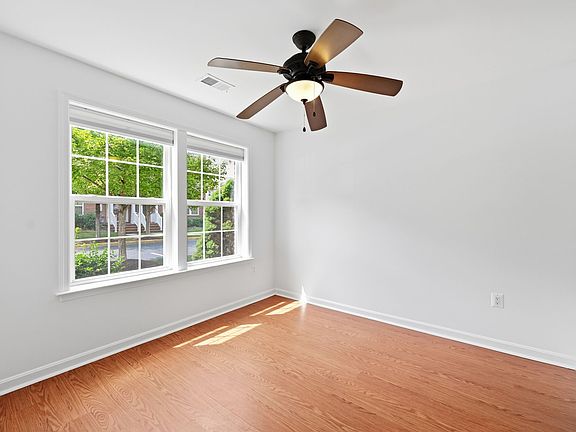 Bright, versatile ground-floor bedroom/home office/gym - flooded with natural light and finished with warm, durable wood-look floors, twin double-hung windows, crisp white trim, and a ceiling fan with light kit.