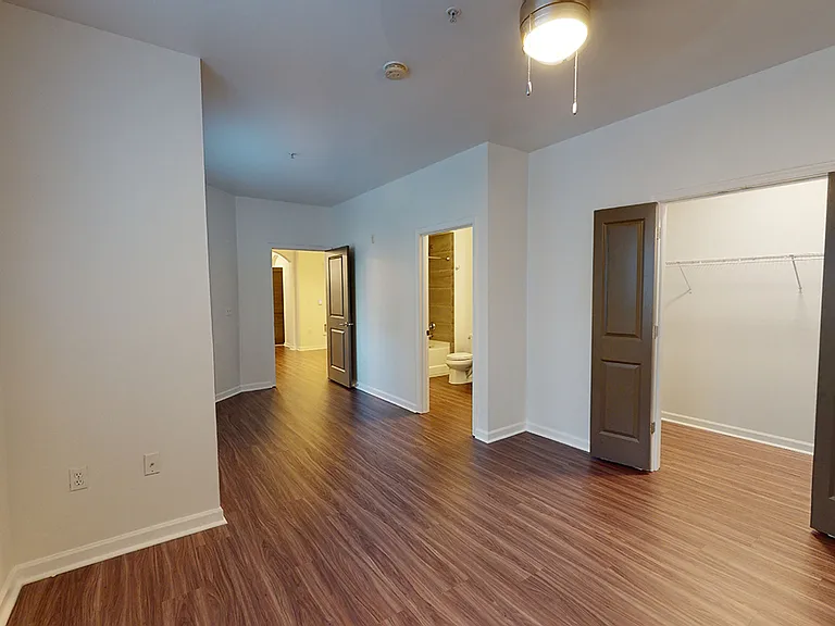 Spacious apartment bedroom with large closet, attached bathroom and wood-style flooring.