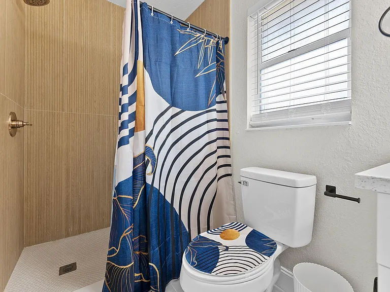 Full bathroom with a walk-in shower, window with blinds for ventilation, and a vanity counter for everyday essentials.