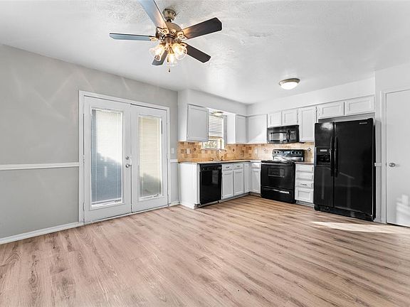 Kitchen with black appliances, light wood-type flooring, ceiling fan, backsplash, and white cabinetry