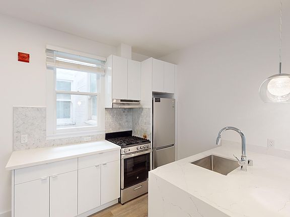 Kitchen with multiple cabinets, refrigerator, stove, range hood, and sink