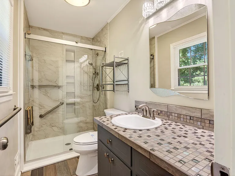 Updated bathroom with glass-enclosed shower, tiled vanity, ample storage, and a window for natural light.