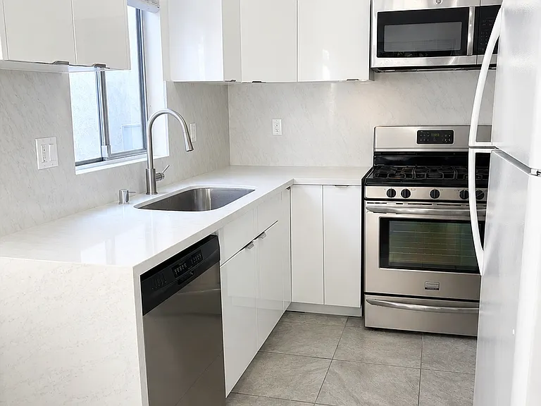 Sleek kitchen with glossy white cabinets, stainless steel gas range, built-in microwave, dishwasher, and tile flooring.