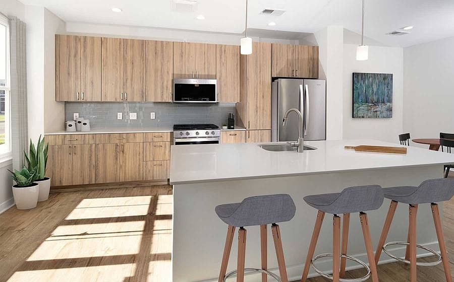 Upgrade Scheme townhome kitchen and dining areas with oak cabinetry, grey tile backsplash, grey quartz countertops, stainless steel appliances, and hard surface flooring