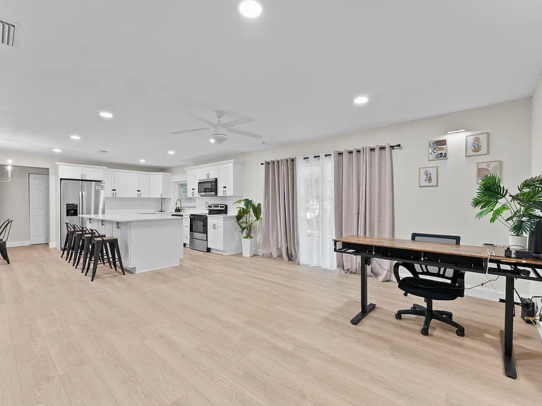 Open-concept kitchen with large island seating, stainless appliances, and wide-plank flooring flowing to a flexible dining/wo