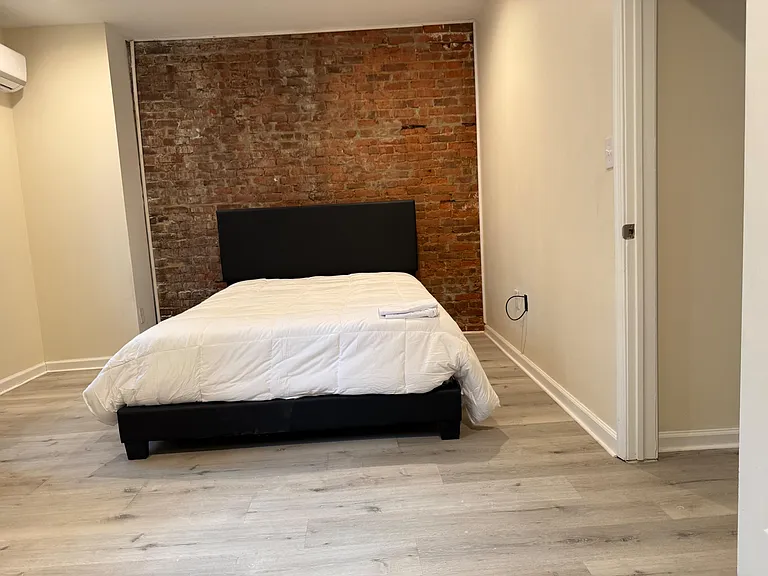 Private bedroom featuring an exposed brick accent wall, wood-style flooring, and ample space for a full bed and essentials.
