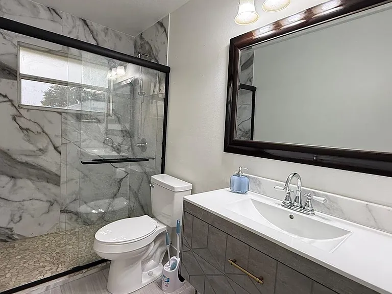 Updated bath with a glass-enclosed walk-in shower, marble-look tile surround, and wide vanity with ample counter space.