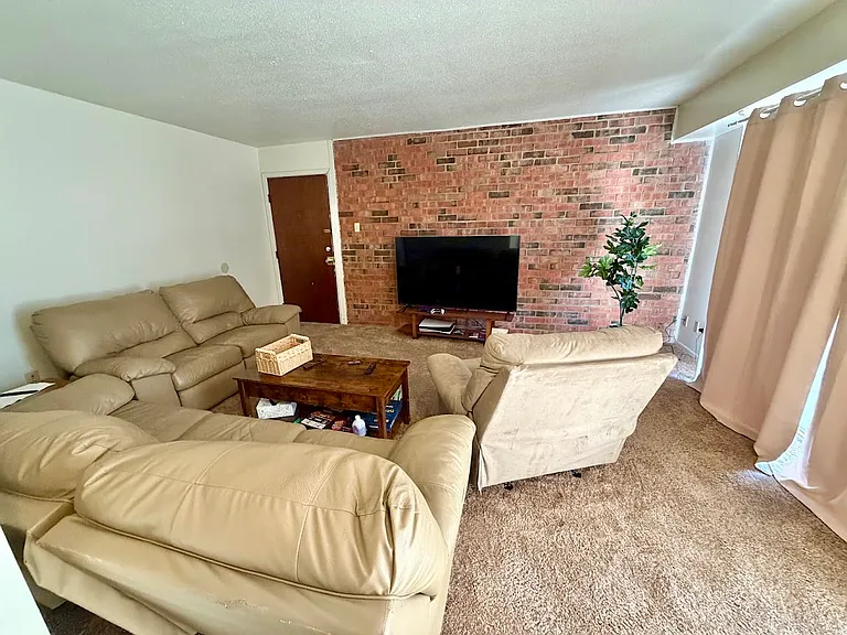 Hunter Ridge Apartments - Spacious living area featuring brick accent wall. Patio/balcony is right off the living room.