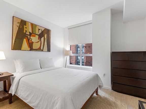 Wake up to natural light in this serene bedroom featuring a plush queen bed and large windows with privacy shades.