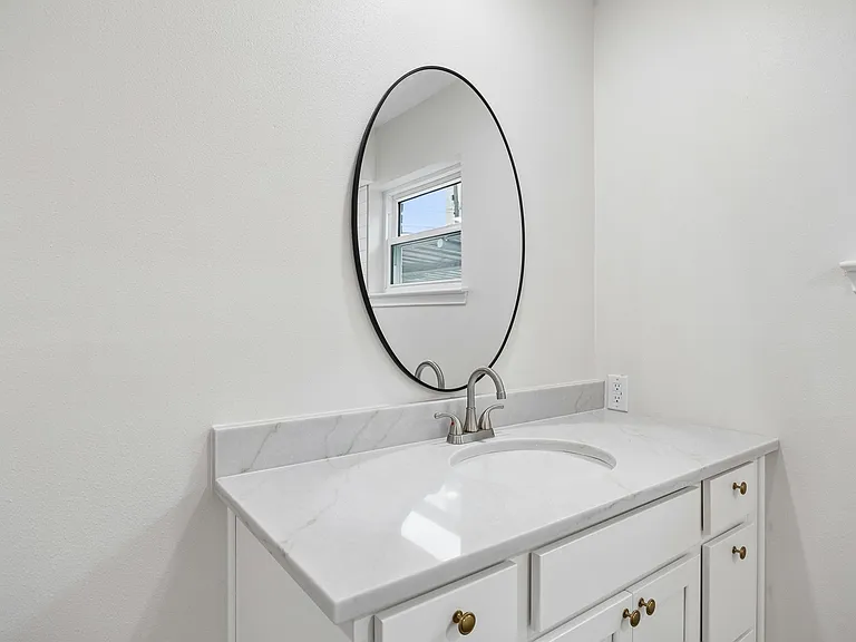 Bathroom vanity featuring a light-toned countertop with integrated sink, brushed nickel faucet, and a black-framed oval mirror