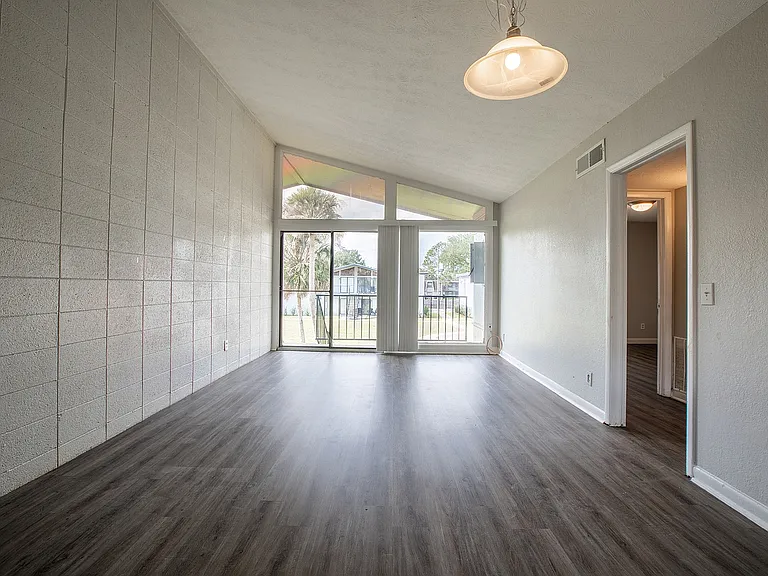 Bright and spacious living room with high ceilings and large windows, offering a view of the lush outdoors. Modern wood flooring enhances the inviting atmosphere.