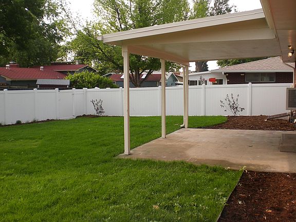 Covered back patio overlooking fenced backyard with sprinkler system
