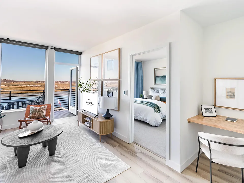 Bright, open living with a dedicated workspace and balcony views just beyond.