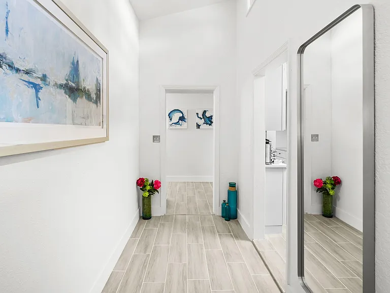 Long, tiled hallway with clean lines, wall art, and space for decorative accents, connecting to adjacent rooms.