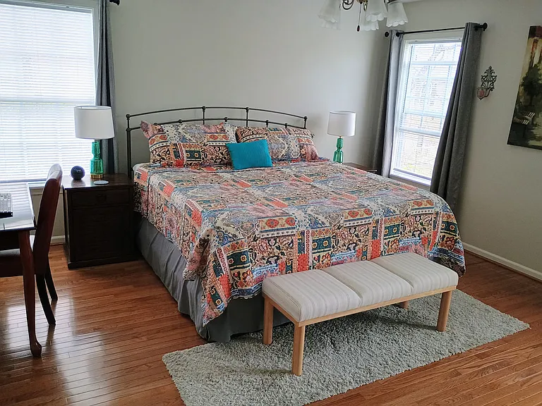 The primary bedroom features a workstation with a desk, chair, keyboard, and two monitors, along with a king size bed and a bench for added comfort. It also includes a small Smart TV.