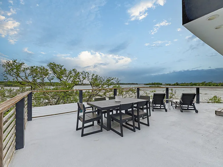 Large outdoor rooftop patio with dining table, lounge seating, and expansive marsh views