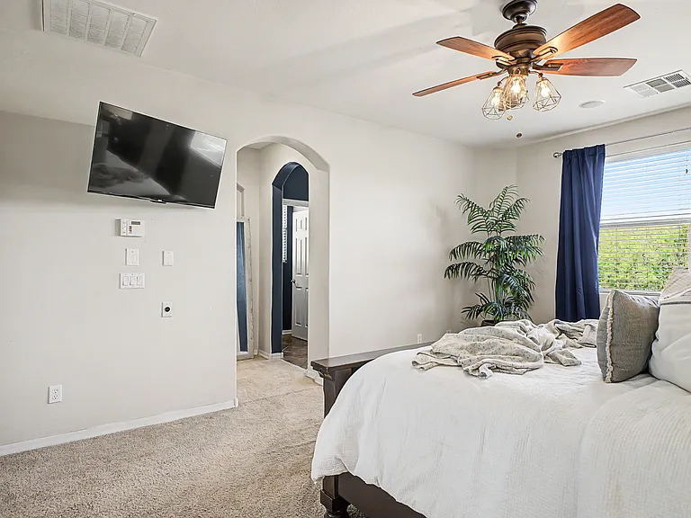 The primary bedroom features a mounted television and an elegant archway leading into the hallway, adding to its charm. From this vantage point, the walk-in closet is located to the left, while the en-suite bathroom is to the right.