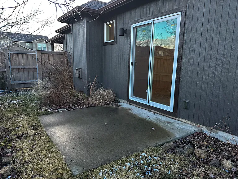Yard on side of home with small patio off family room. Yard wraps around on three sides of home with fruit trees and beautiful annual plants.
