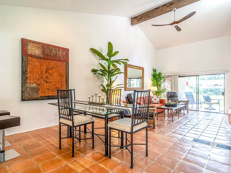 Open-concept dining and living space with soaring ceilings, exposed beam detail, Saltillo tile floors, and natural light throughout. Seamless flow to the patio creates an airy indoor-outdoor setting ideal for entertaining and extended desert stays.