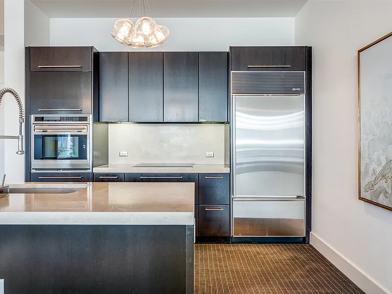 Kitchen featuring appliances with stainless steel finishes, modern cabinets, hanging light fixtures, light stone countertops, and dark brown cabinets