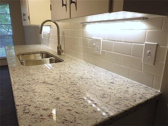 Modern kitchen features granite countertops, subway tile bac