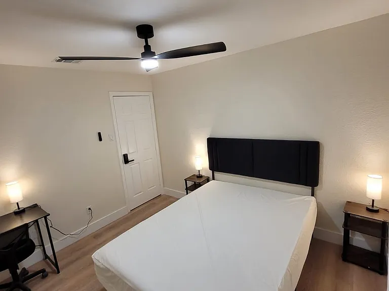 Furnished bedroom with a full bed, nightstands with lamps, and a small desk workspace, plus a ceiling fan for comfort.