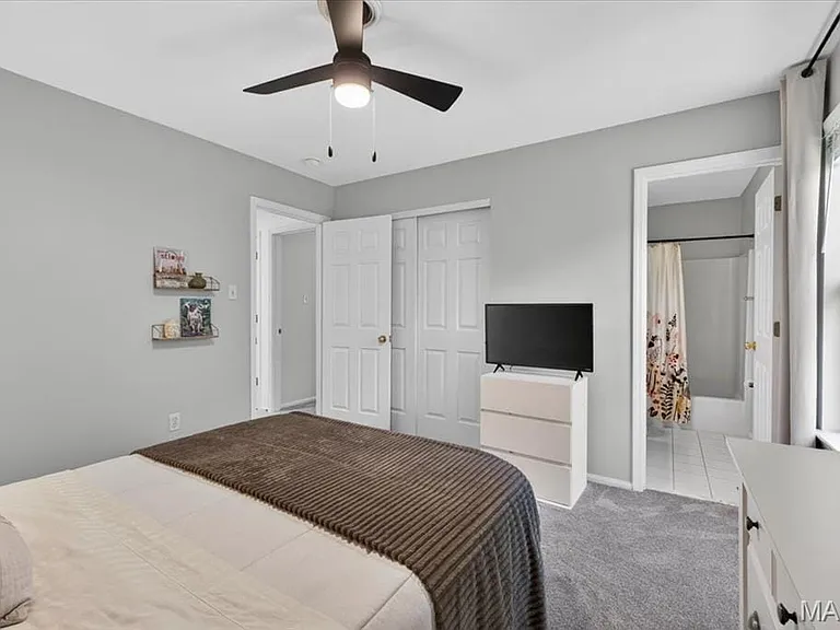 Light gray walls complement the gray carpeting in this bedroom featuring a ceiling fan with integrated lighting