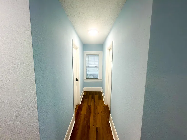 Freshly painted hallway with durable wood-look flooring, overhead lighting, and a window at the end for added daylight.