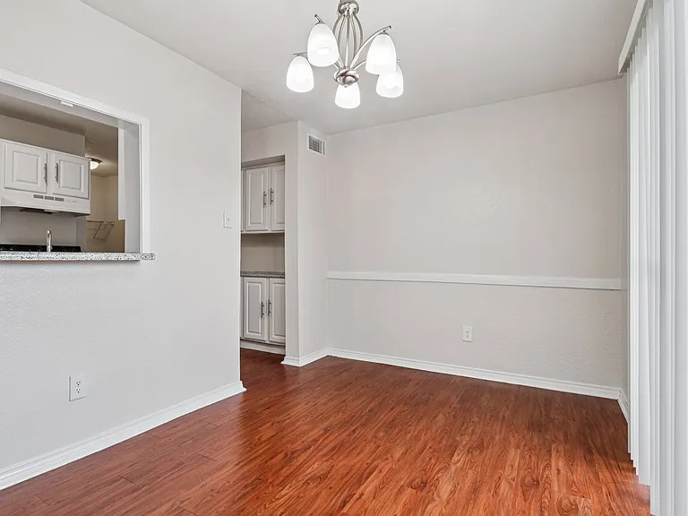Bright dining area with elegant chandelier and open access to a modern kitchen, featuring warm wood-style floors and sleek white cabinetry. Bright dining area with elegant chandelier and open access to a modern kitchen, featuring warm wood-style floors an