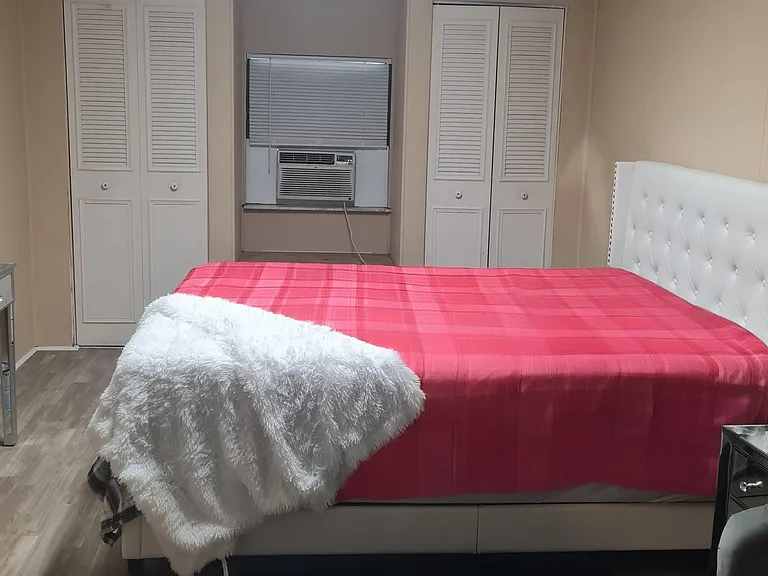 Furnished bedroom with a large bed, mirrored dresser, and dual closets, plus a window A/C unit for comfort.
