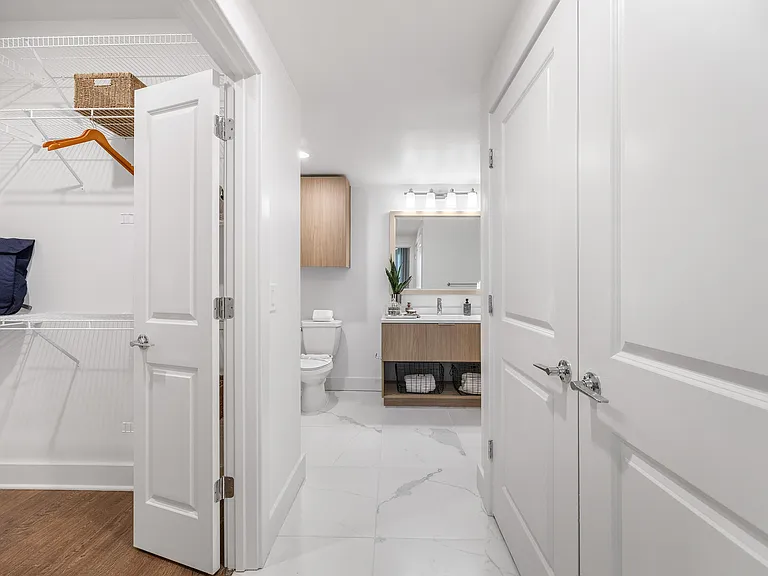 Modern apartment bathroom with elegant vanity, stylish cabinet, and spacious walk-in closet featuring wooden flooring.