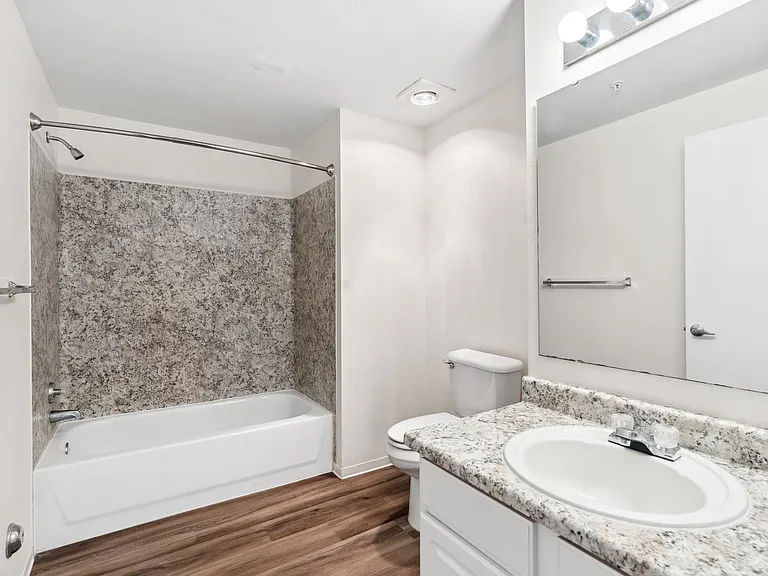 Clean, modern bathroom featuring a tub/shower combo, granite-style countertops, and bright lighting.