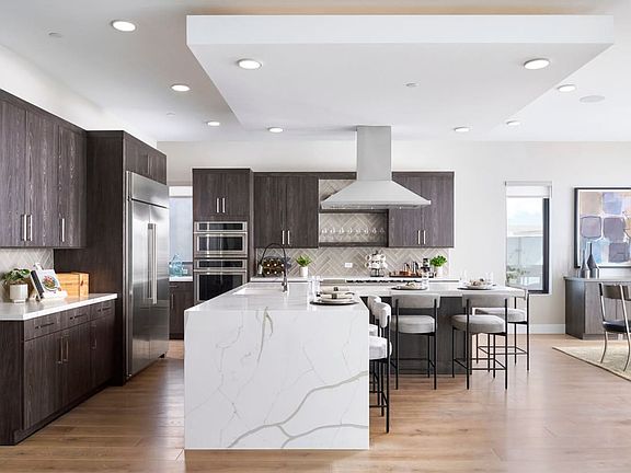 A modern, open-concept kitchen with dark wood cabinets, a large white marble island, and stainless s