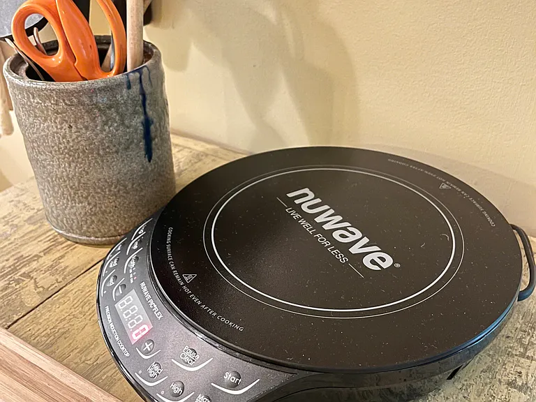 Induction hot plate, kitchen utensils, and cutting board with pans and pot for cooking at home.