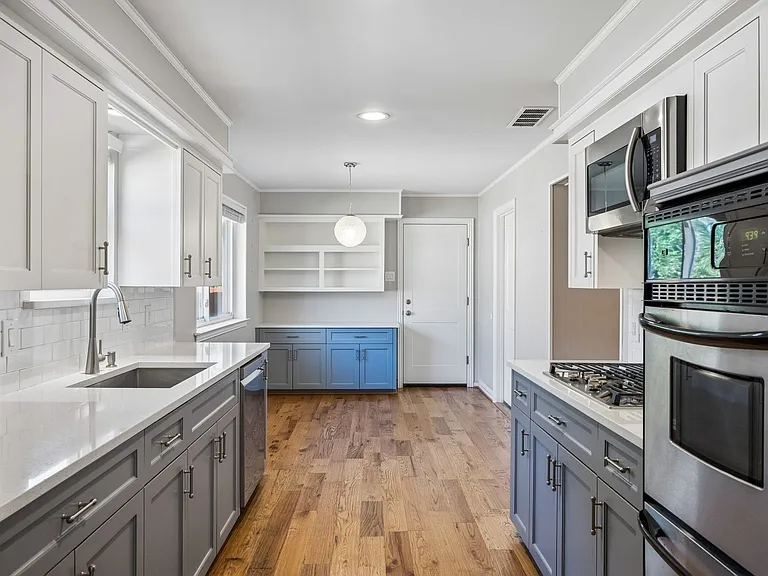 Galley kitchen featuring white upper cabinetry, gray lower cabinetry, and wood-finish flooring