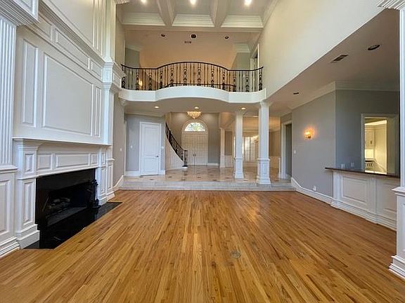 Unfurnished living room with ornamental molding, light wood-type flooring, decorative columns, beamed ceiling, and a fireplace