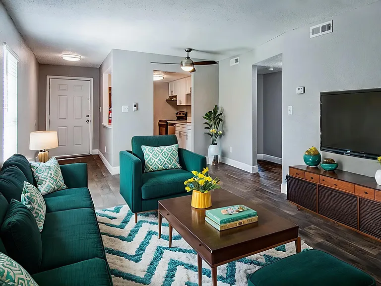 Inviting living room with elegant teal furnishings, a modern patterned rug, and warm natural light creating a cozy ambiance.