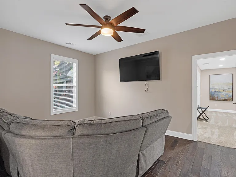Comfortable living area with ceiling fan, wall-mounted TV, and a large sectional, plus easy access to the hallway.