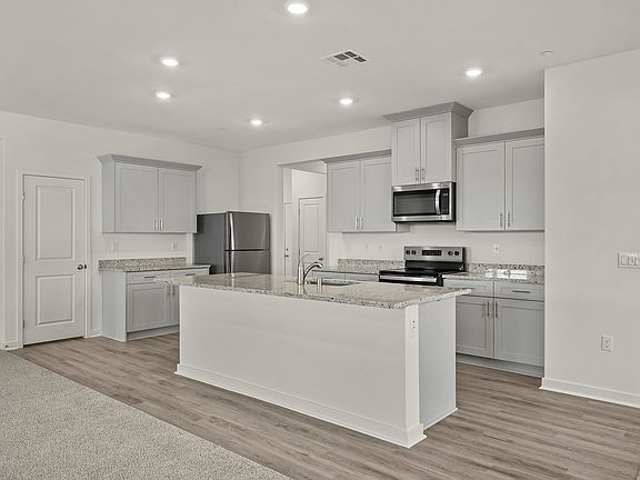 The kitchen has stainless steel appliances and plank flooring.