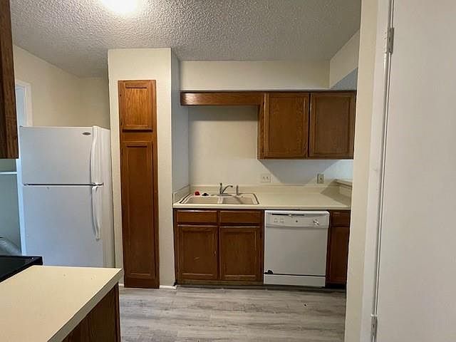 Kitchen with white appliances, light wood-style flooring, light countertops, and a textured ceiling