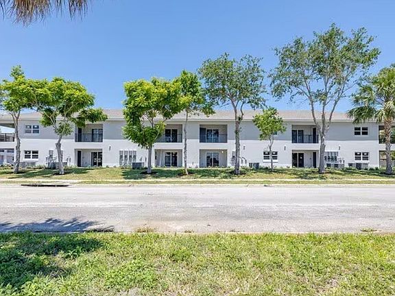 Inviting two-story apartment complex surrounded by lush greenery and shaded by mature trees, offering a serene and welcoming atmosphere.