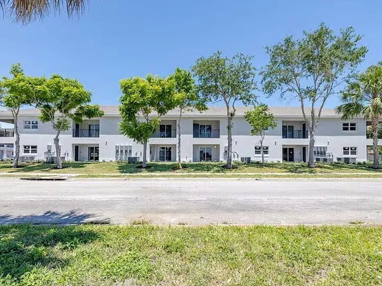Inviting two-story apartment complex surrounded by lush greenery and shaded by mature trees, offering a serene and welcoming atmosphere.